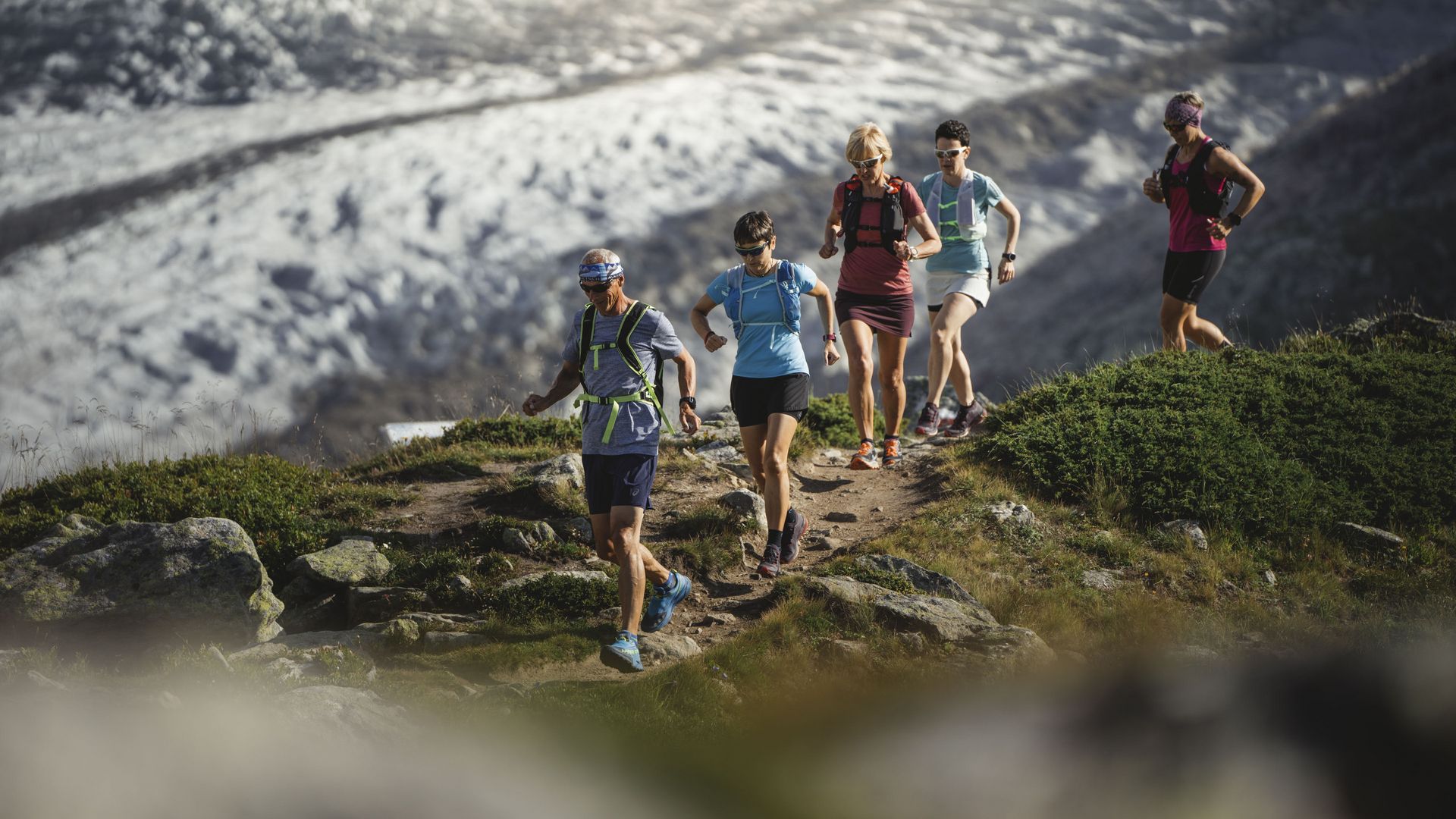 Cinq coureurs de trail courent le long d'un étroit sentier de montagne pour des offres sportives de groupe Aletsch Arena.