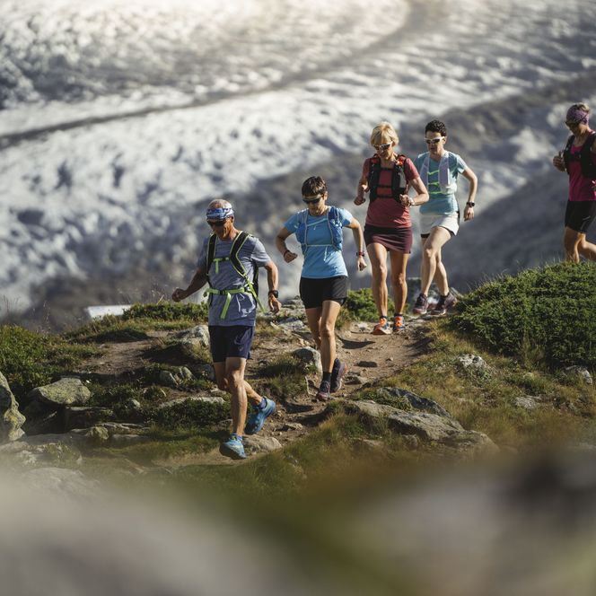 Fünf Trailrunner rennen einen schmalen Bergpfad entlang für sportliche Gruppenangebote Aletsch Arena.