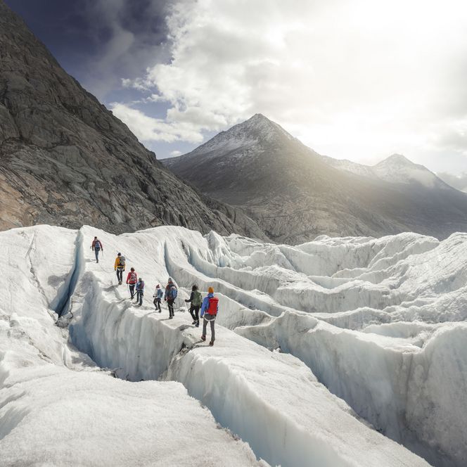 Hikers on the white ice. In the background, the sun shines majestically bright over the Grosser Aletsch Glacier.