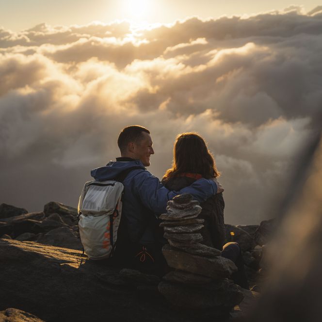 Un couple est assis sur l'Eggishorn près de Fiesch en Suisse et observe le lever du soleil au-dessus d'une mer de nuages.