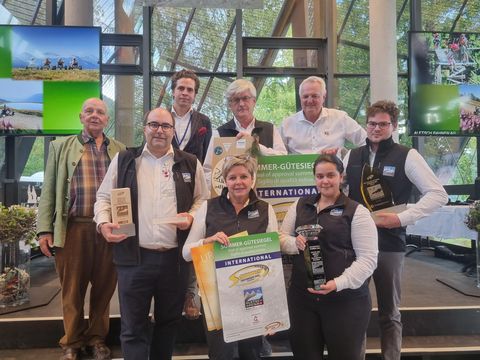 Auszeichnungen Aletsch Arena: Gruppe mit Sommer-Gütesiegeln und Trophäen vor grossen Fenstern.