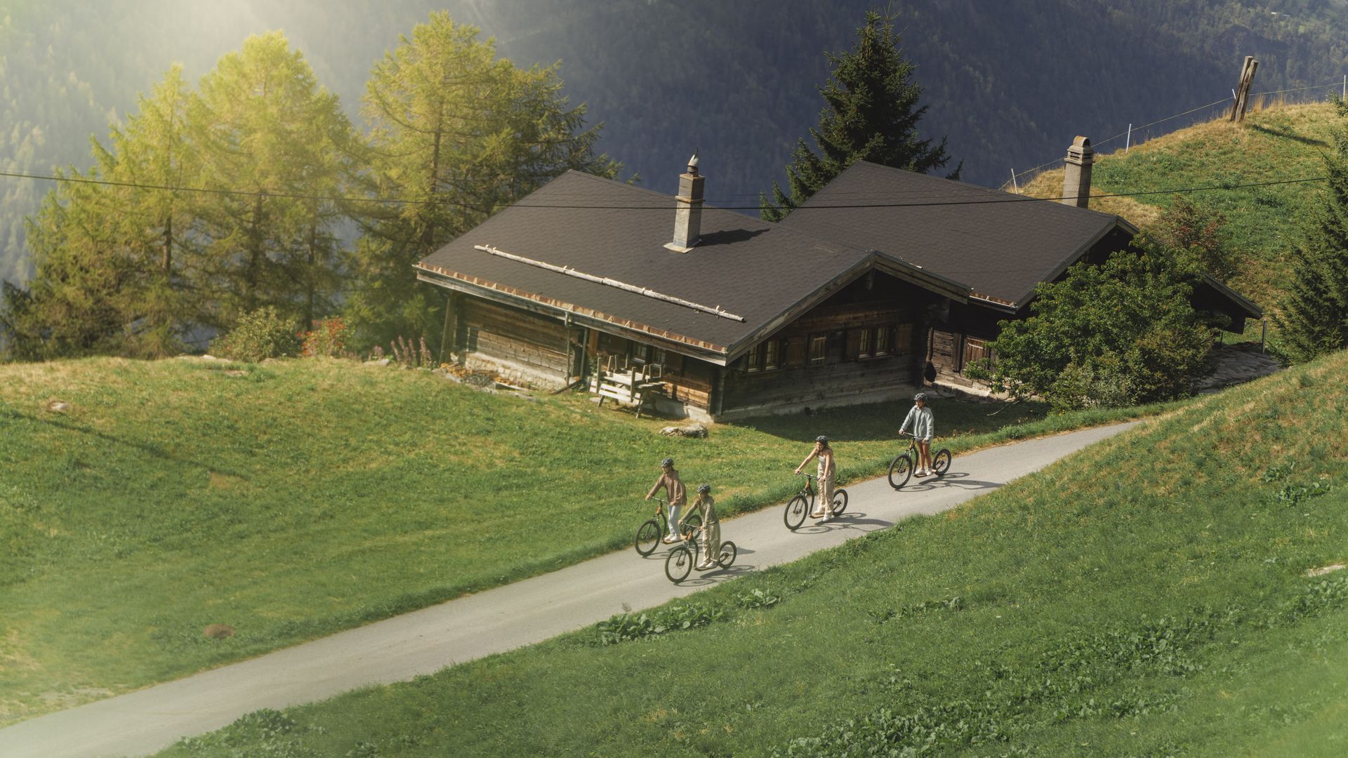 Als Alternative zum Mountaincart Aletsch Arena fahren Mädchen auf Trottinetten an einem urigen Holzchalet vorbei.