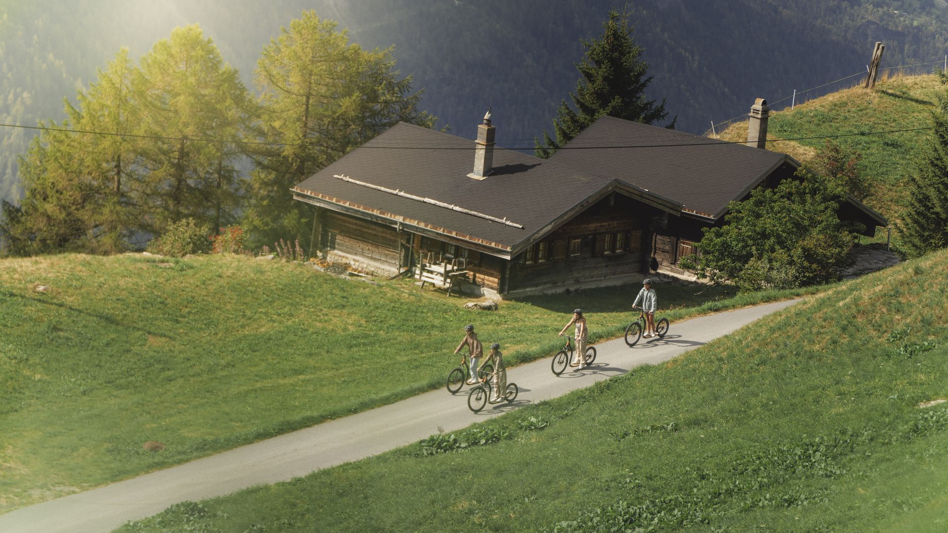 Comme alternative au mountaincart Aletsch Arena, les filles passent en trottinette devant un chalet en bois rustique.
