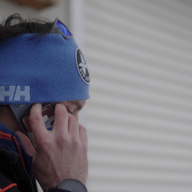 Jobs Aletsch Bahnen AG: Nahaufnahme einer Person der Pistenrettung mit blauem Stirnband beim Telefonieren.