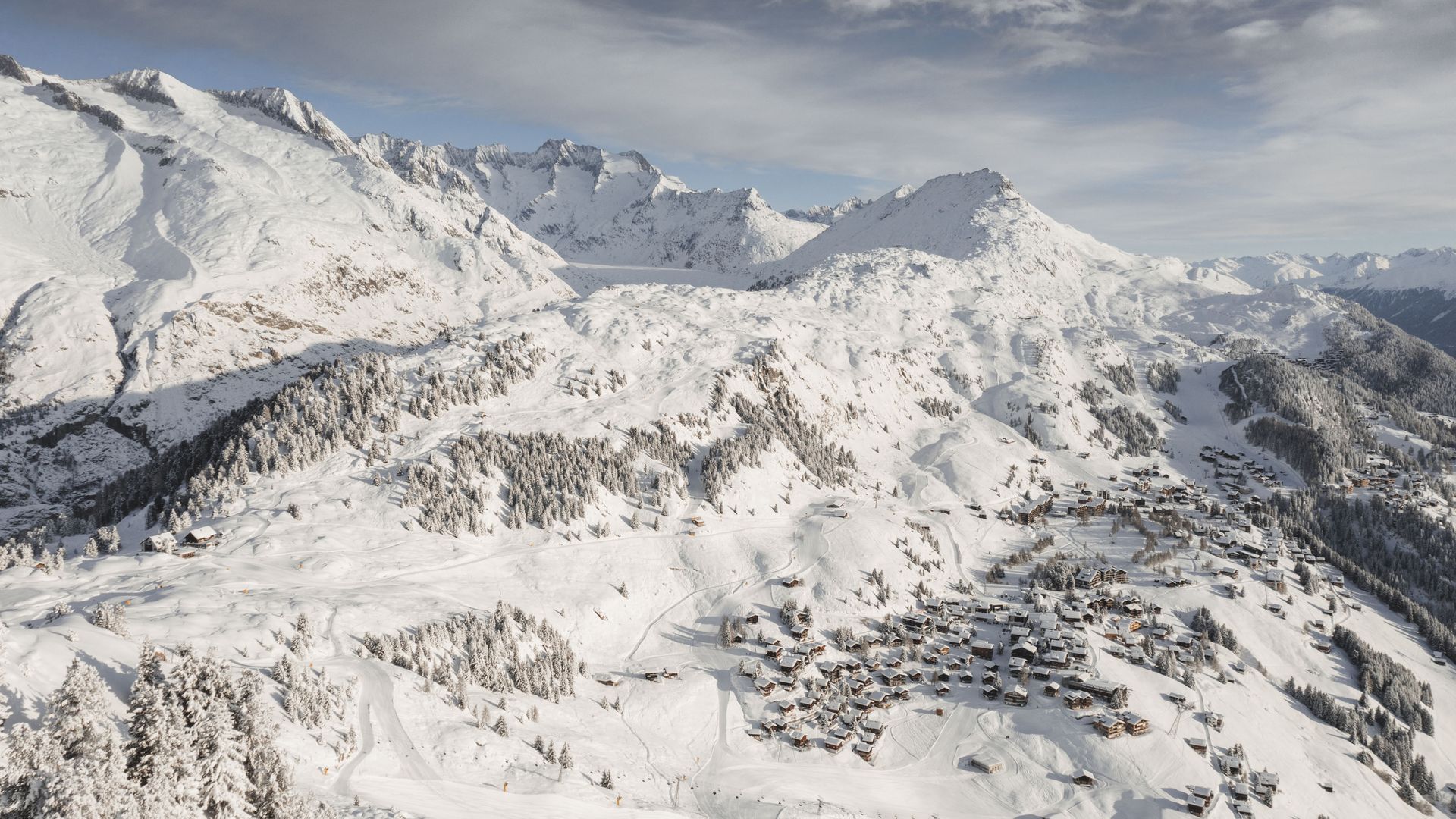 Une large vue aérienne montre le village profondément enneigé de Riederalp Suisse, entouré de pistes de ski et de sommets alpins marquants.