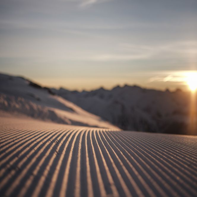 Gros plan sur les sillons typiques d'une piste fraîchement préparée par un lever de soleil lumineux dans l'hiver de l'Aletsch Arena.