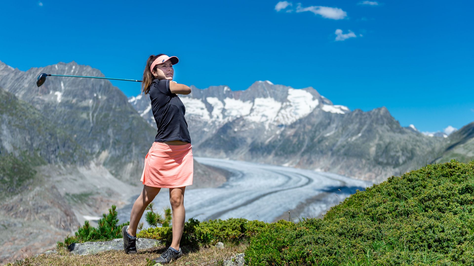 Une golfeuse suit son coup de départ face au grand glacier d'Aletsch et découvre les joies du golf à Riederalp, dans un cadre alpin spectaculaire.